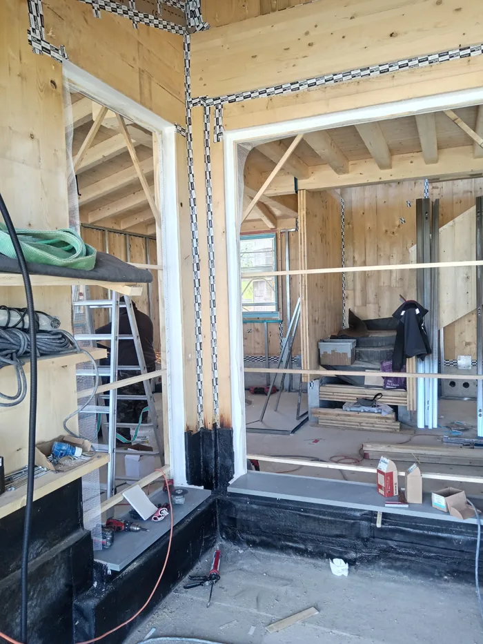 Fasi della costruzione di una casa ecologica: cantiere in legno con fori finestra nastrati e impermeabilizzati