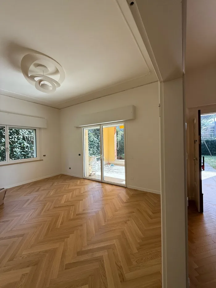 Soggiorno con parquet a spina di pesce e serramenti bianchi affacciati sul giardino