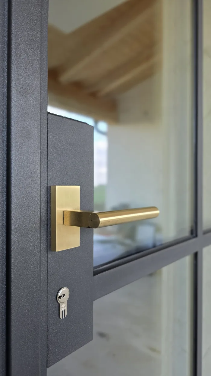 Dettaglio serratura e cilindro di sicurezza con maniglia in ottone su porta blindata in alluminio antracite