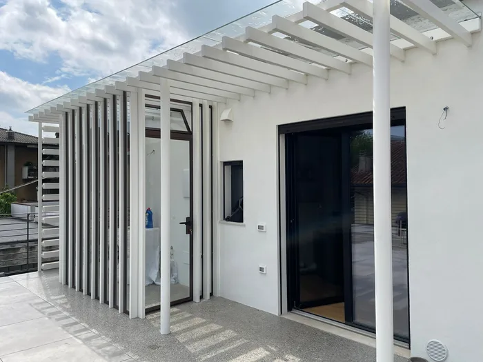 Pergola bianca con copertura in vetro su terrazzo, senza aumento di volumetria
