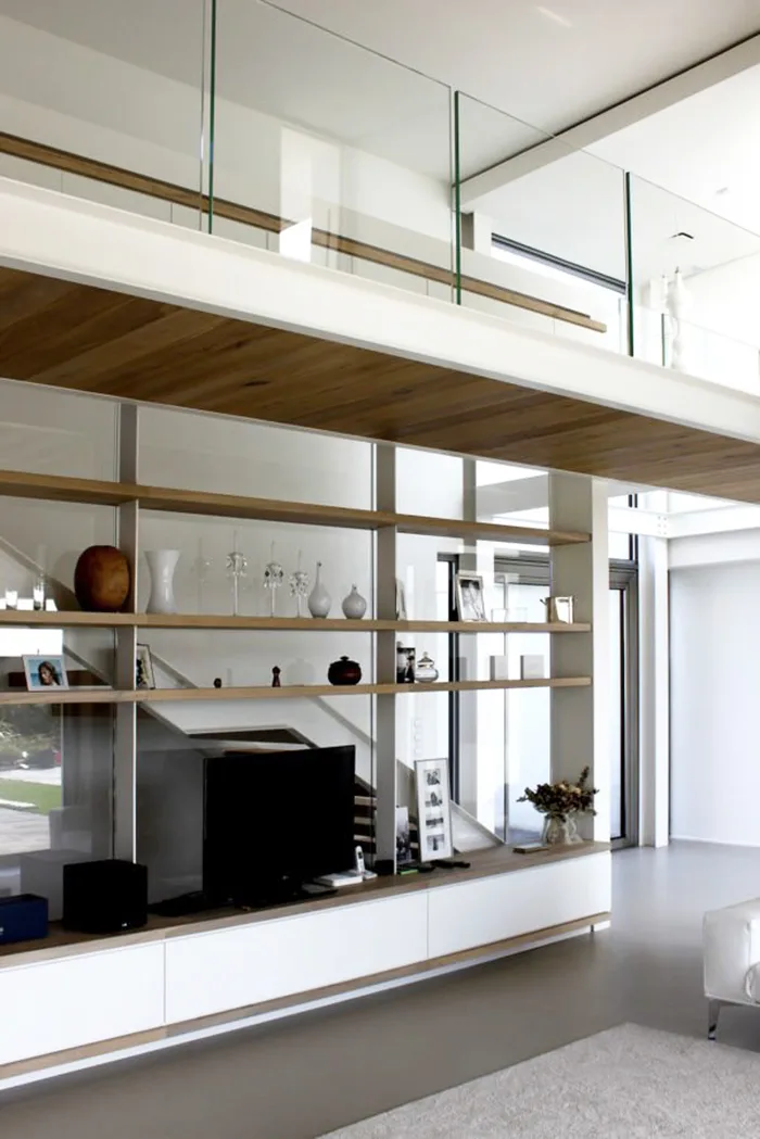 Soppalco in casa con parapetto in vetro sopra libreria a vista sul soggiorno