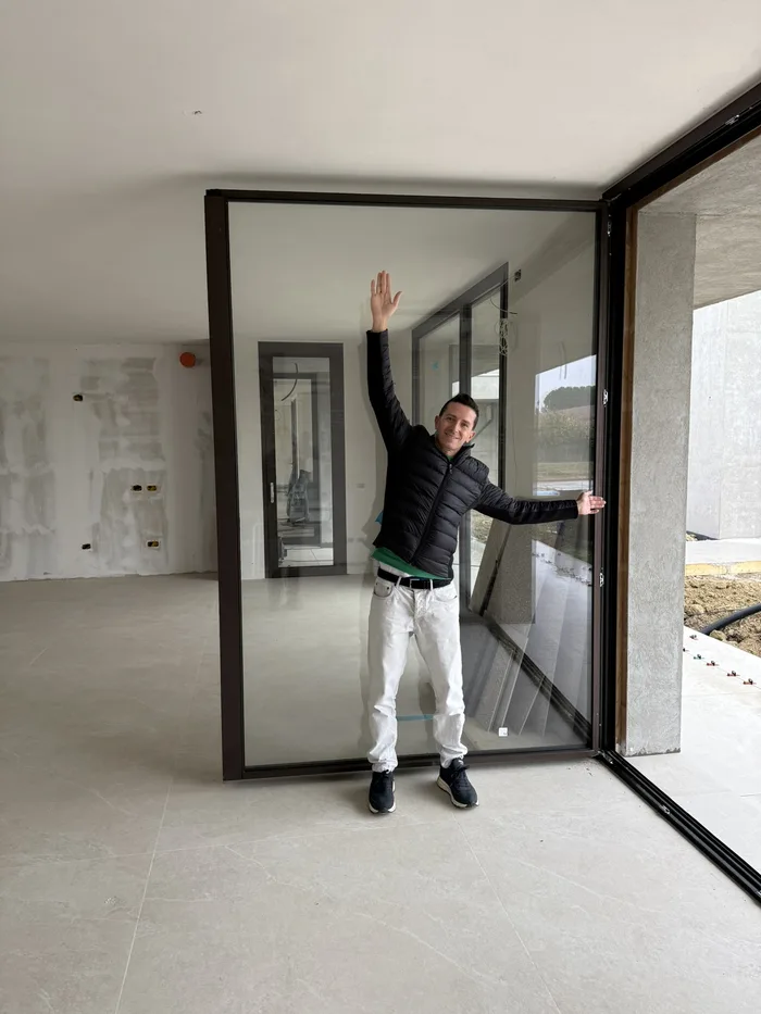 William Bisacchi in cantiere accanto a una grande anta vetrata