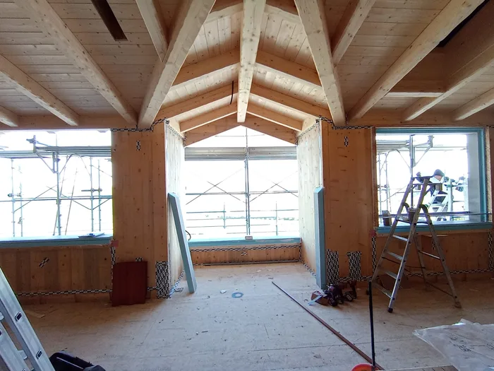 Interno di casa in legno con capriate e finestre bianche appena posate in cantiere