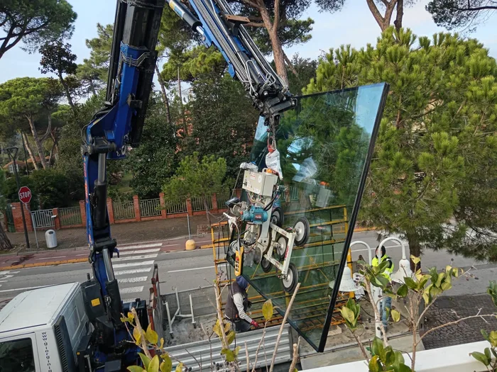 Lastra di vetro stratificato sollevata con gru e ventose durante la posa in cantiere