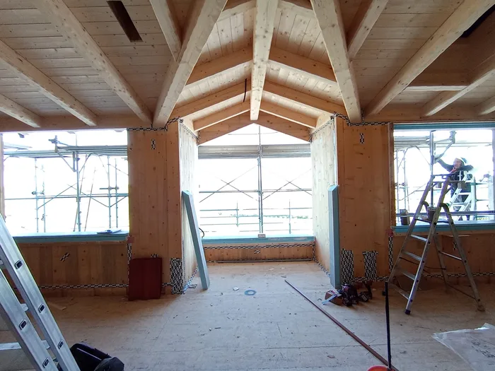 Interno di casa in legno con capriate e finestre in fase di posa in cantiere